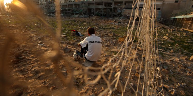TOPSHOT - Palestinian runner and football player Bilal Abu Samaan, 20, sits in the rubble of the bombed Palestine Stadium in Gaza City on November 28, 2012. The stadium was bombed by the Israeli airforce during a conflict between the ruling Hamas party and the Israeli military between 14 and 21 November 2012. AFP PHOTO / PATRICK BAZ (Photo by PATRICK BAZ / AFP) (Photo by PATRICK BAZ/AFP via Getty Images)